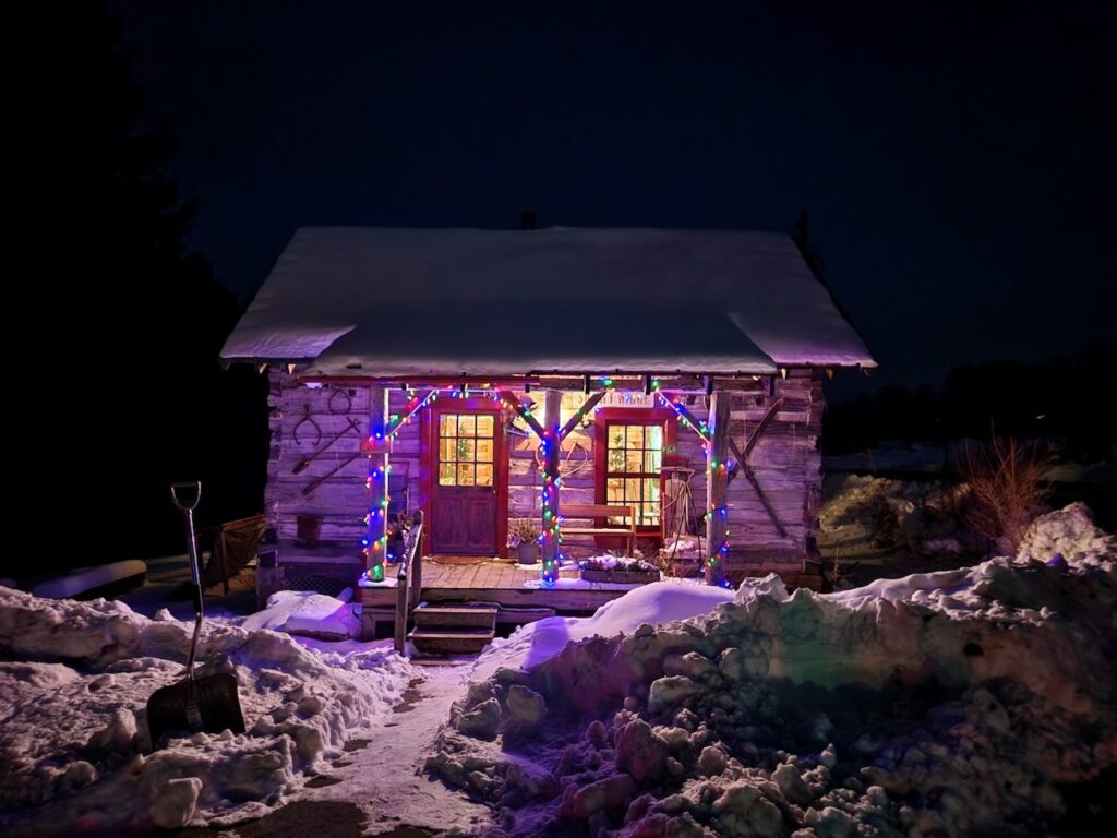 a lit from within cozy cabin decorated with christmas lights that give it a purple glow
